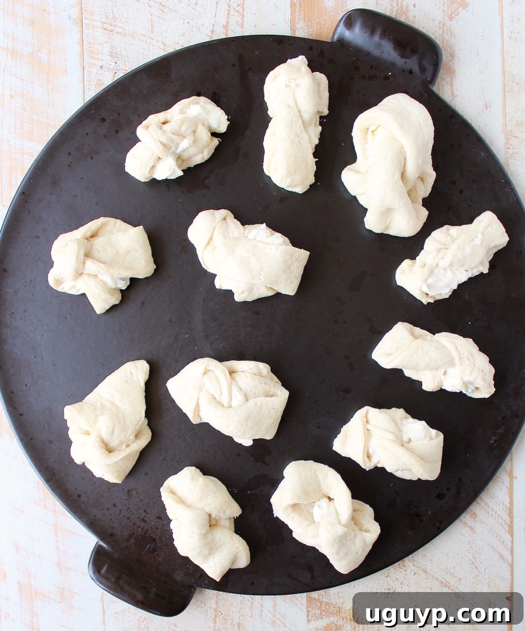 Dough strips filled with cheese being tied into knots and placed on a baking sheet.