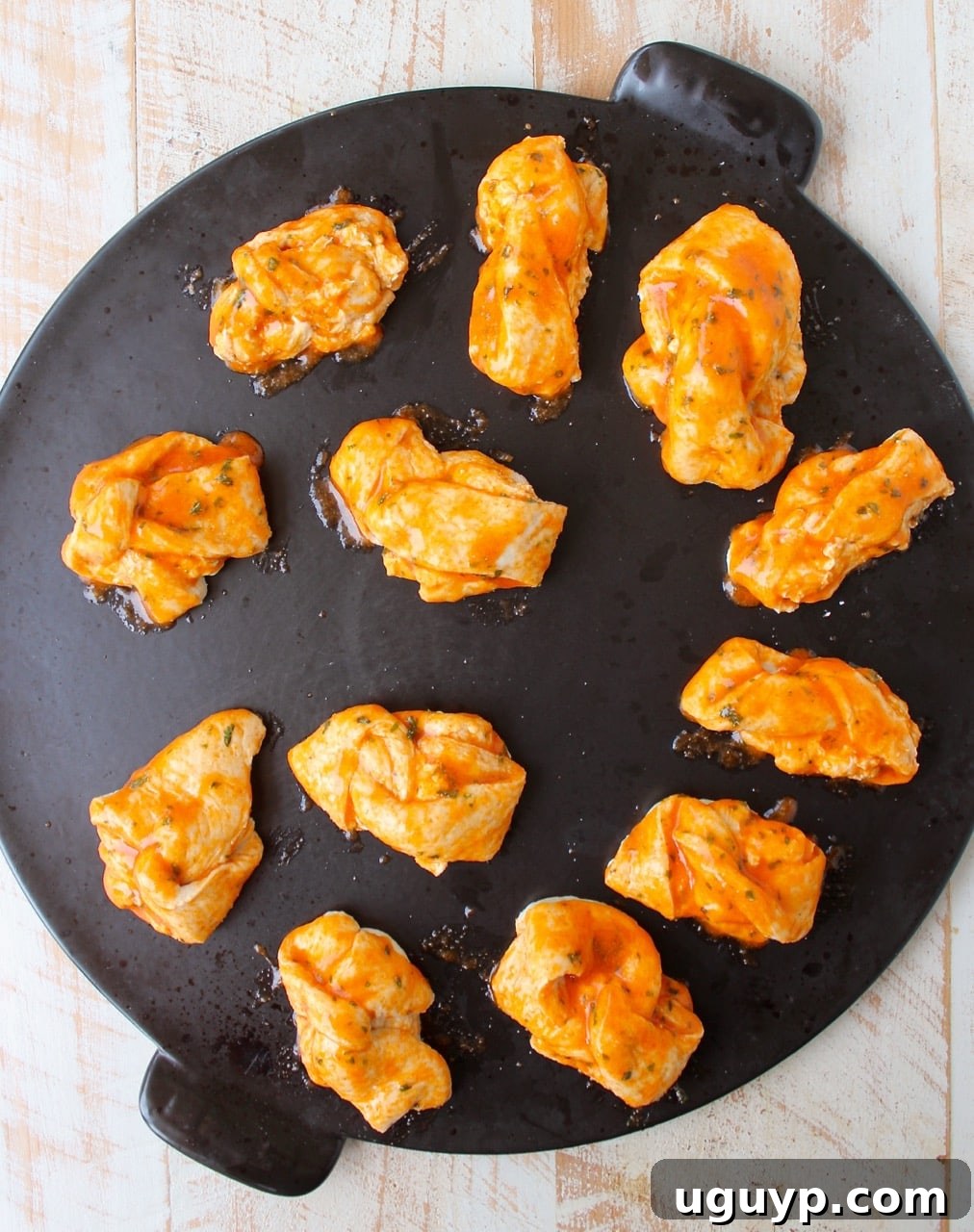 Cheesy garlic knots on a baking sheet, brushed with buffalo garlic butter, ready for the oven.