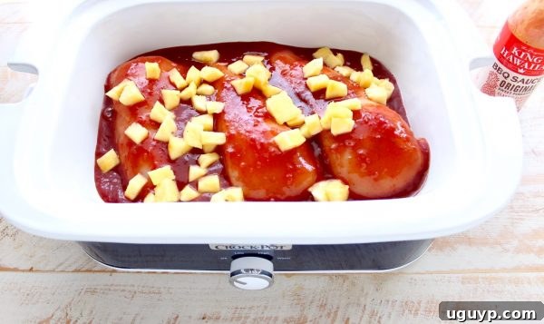 Chicken breasts, pineapple, and BBQ sauce being added to a slow cooker pot.