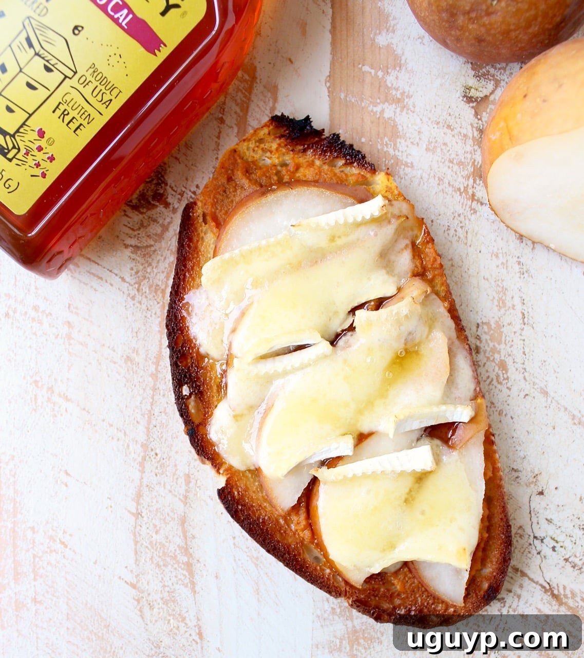 A close-up shot of a slice of pumpkin toast topped with melted brie cheese, thinly sliced pears, and a drizzle of honey, on a rustic board.