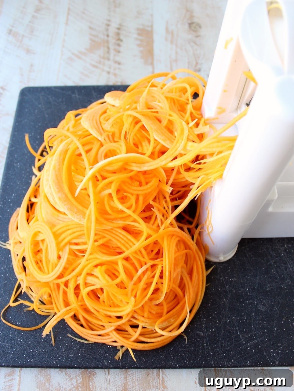 butternut squash noodles coming out of a spiralizer machine onto a cutting board