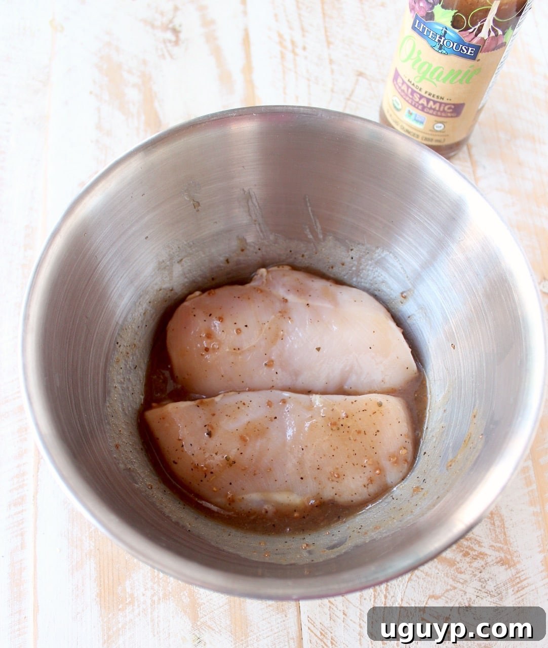 raw chicken breasts covered in balsamic vinaigrette dressing in a metal bowl