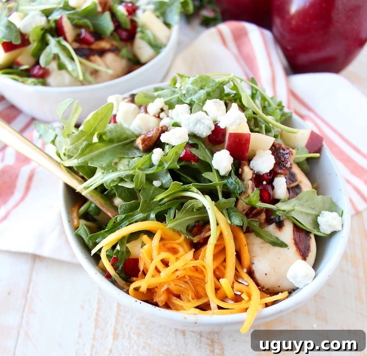 butternut squash noodles, arugula salad with diced apples and grilled chicken in a bowl with a fork