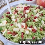 Brussels Sprout Salad with Honey Dijon Dressing, garnished with diced apples and pomegranate seeds in a rustic bowl.