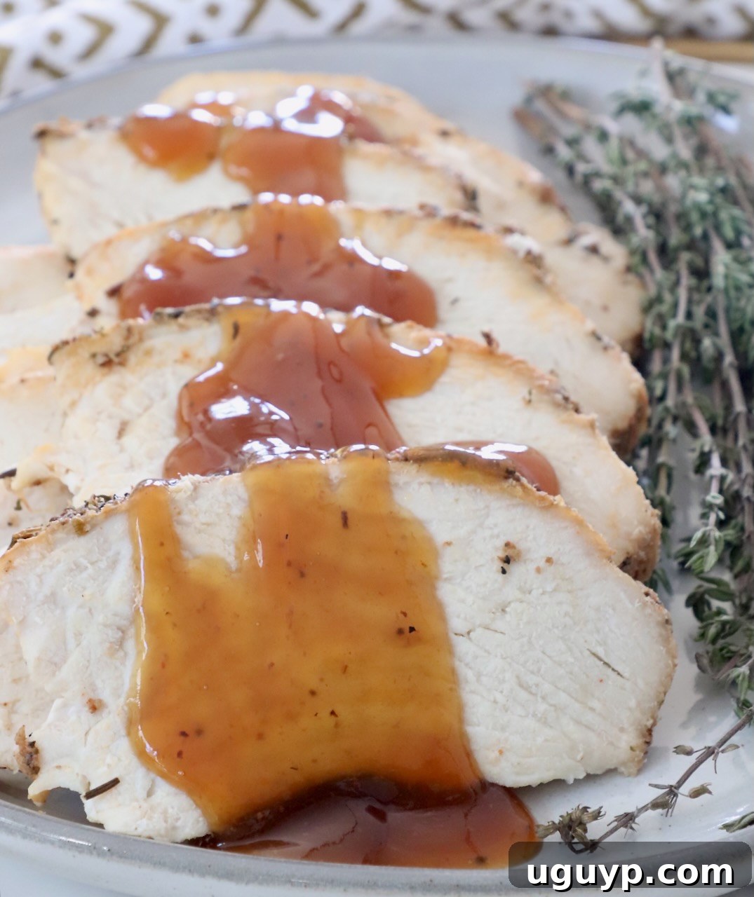 Slices of turkey on a plate with a maple apple glaze drizzled over the turkey, garnished with fresh herbs