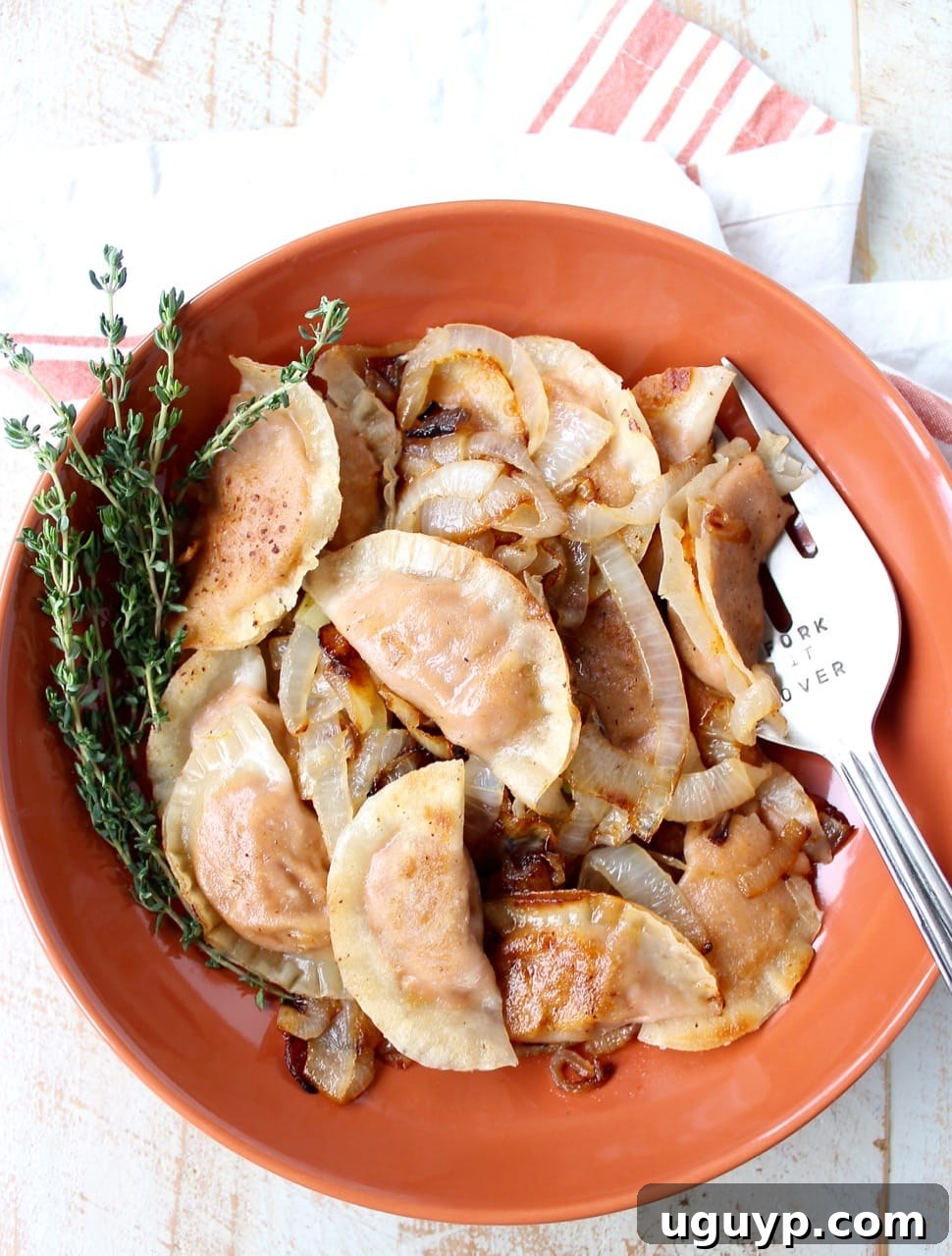 Cooked sweet potato pierogies with caramelized onions and fresh thyme in an orange bowl, ready to be served