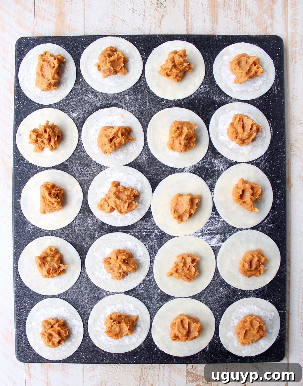 A spoonful of mashed sweet potatoes being placed onto a wonton wrapper, illustrating the filling process for pierogies