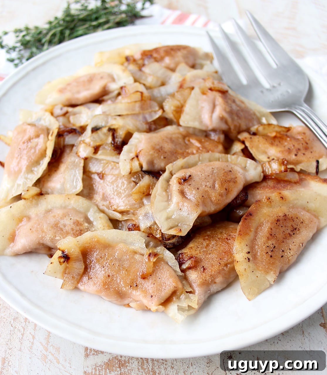 Finished sweet potato pierogies served with caramelized onions in an orange bowl, garnished with fresh herbs