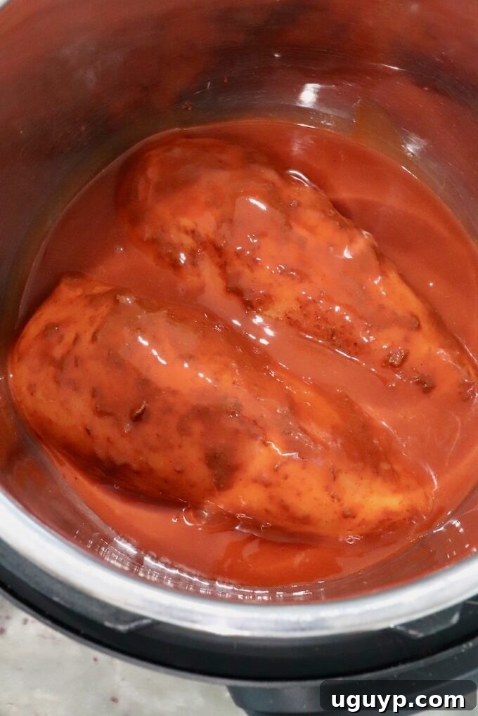 Seasoned chicken breasts, generously covered in buffalo sauce, sitting in an Instant Pot.