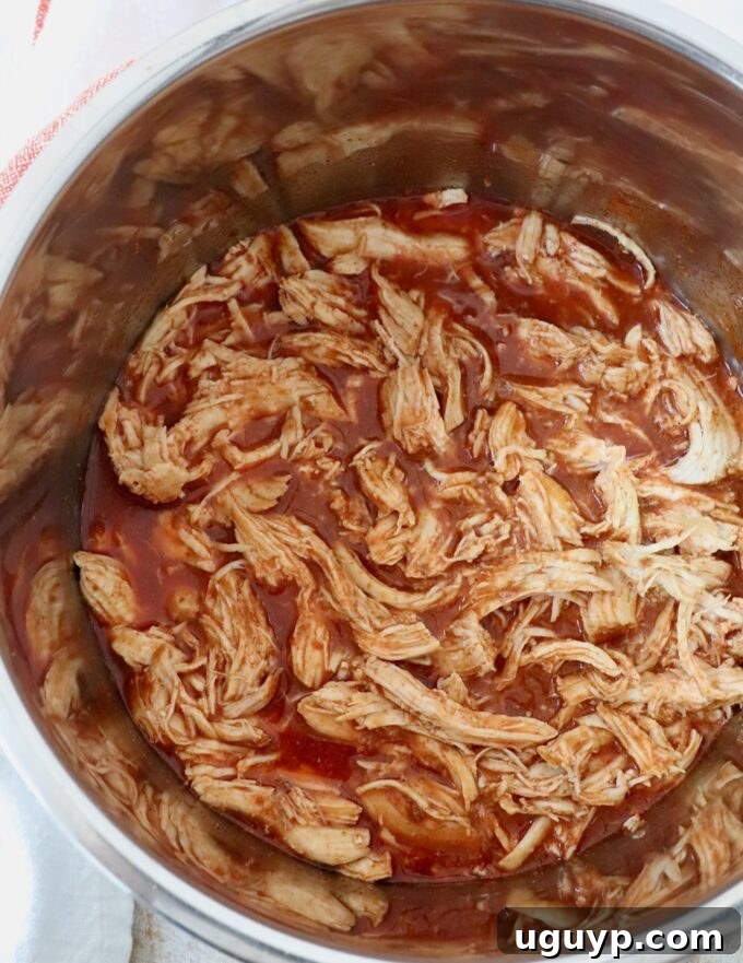 Cooked and perfectly shredded buffalo chicken visible inside the Instant Pot, bathed in sauce.