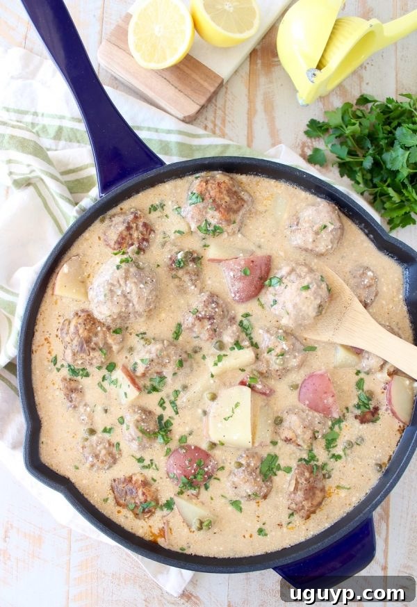 Close-up of German meatballs and potatoes simmering in a creamy caper sauce in a pot.