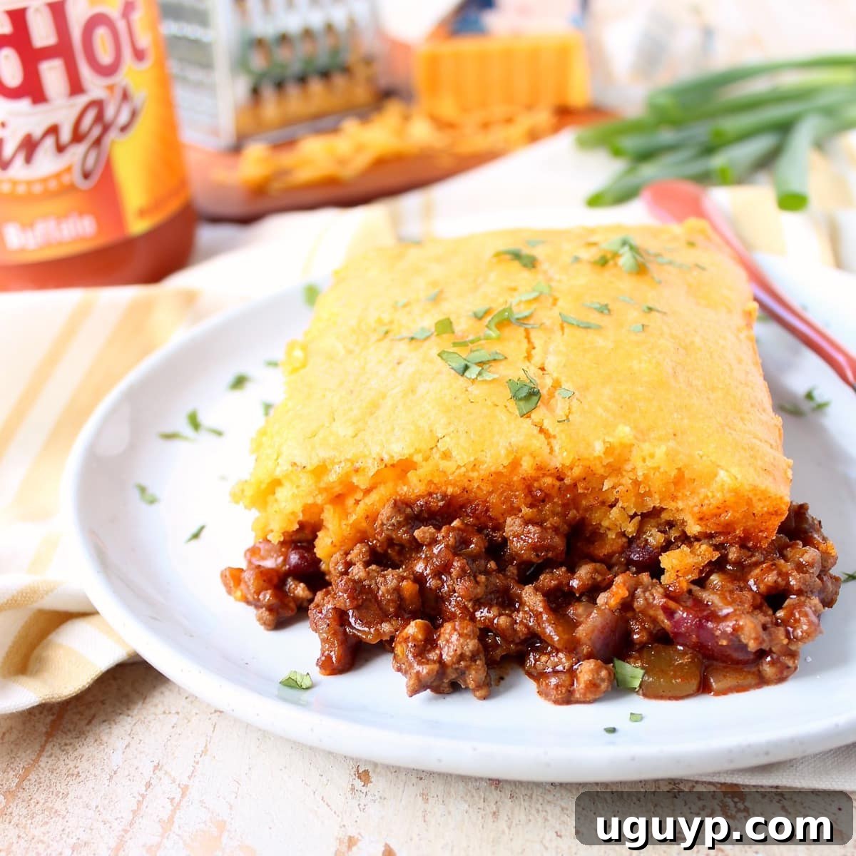A generous slice of Buffalo Cheddar Cornbread Chili Pie served on a white plate with a fork, showcasing the layers of chili and golden cornbread.