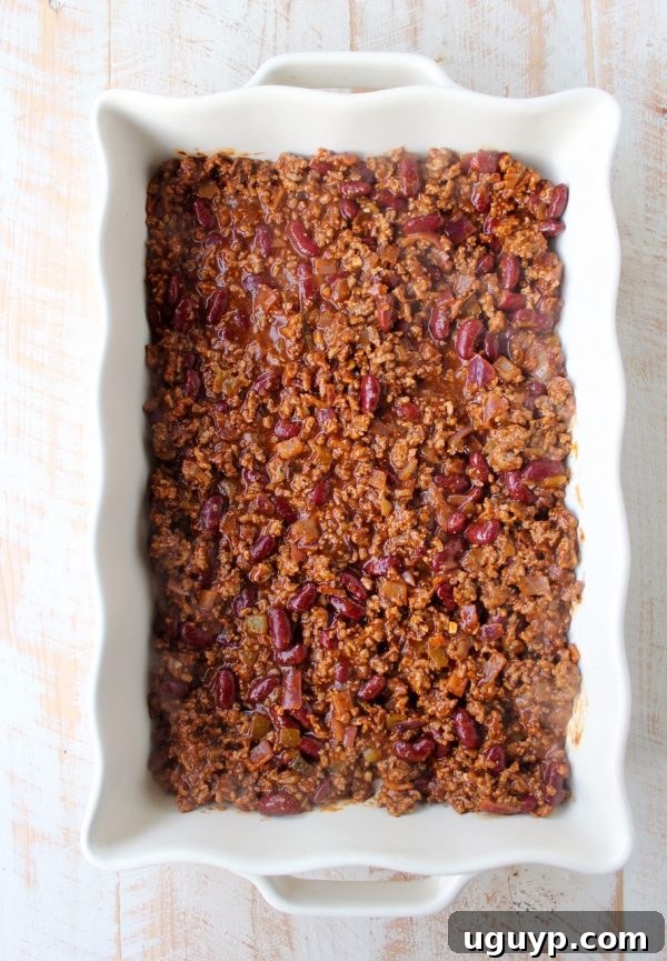 Rich, savory chili bubbling gently in a rectangular casserole dish, forming the base of the pie.