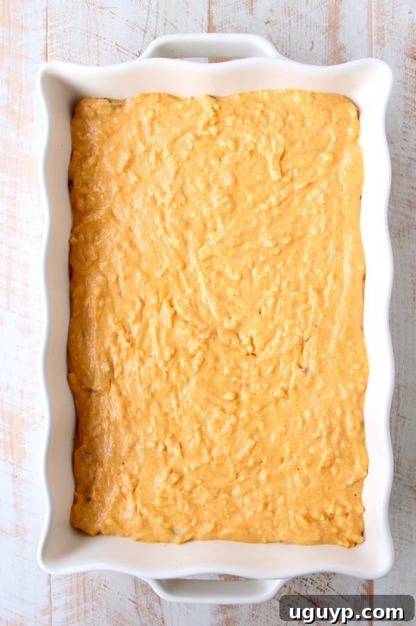 The vibrant chili base in the casserole dish, now topped with the creamy, uncooked cornbread mixture, ready for baking.