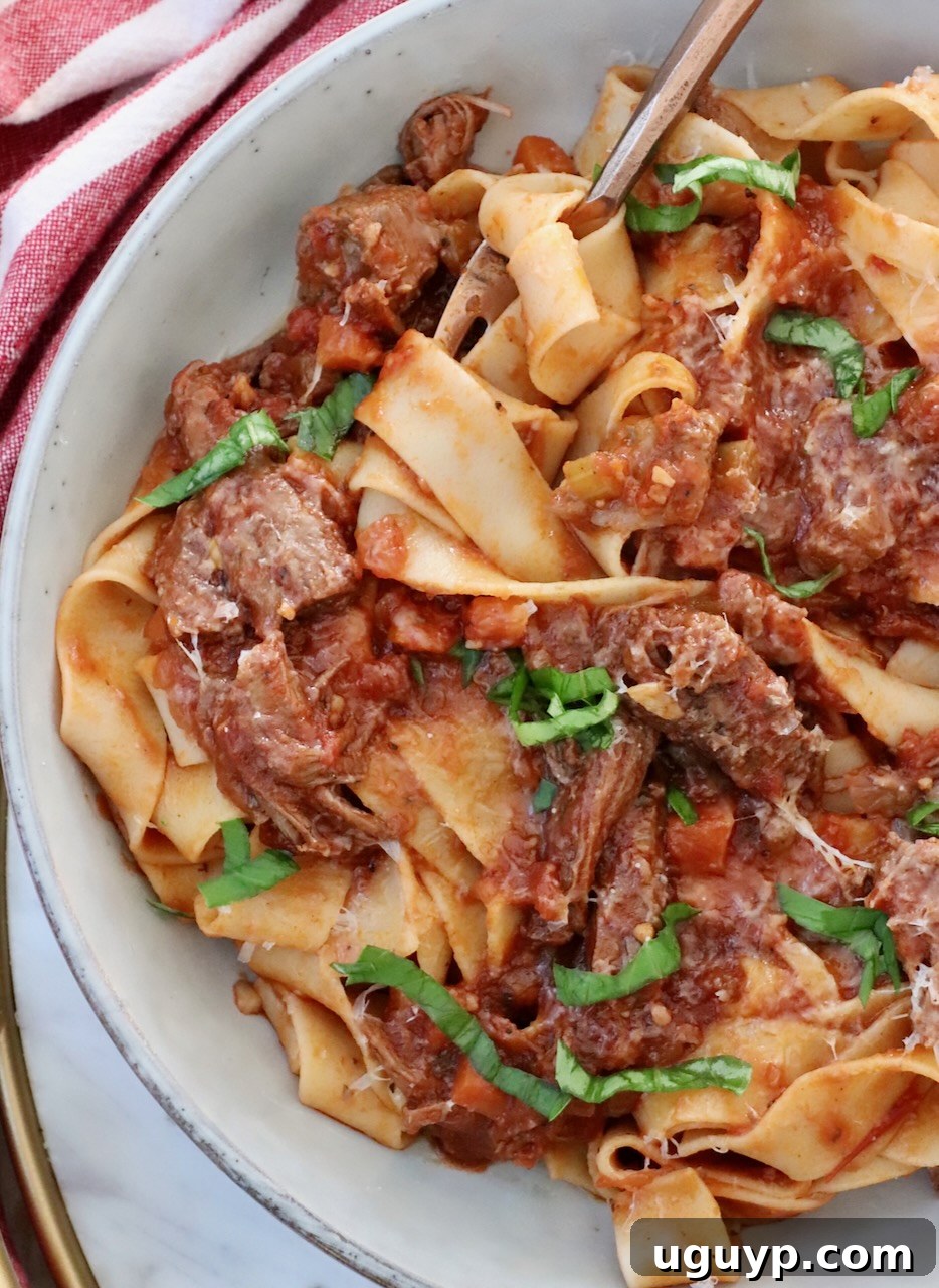 Hearty Instant Pot Beef Ragu sauce tossed with wide pappardelle pasta in a rustic bowl, ready to be enjoyed with a fork.