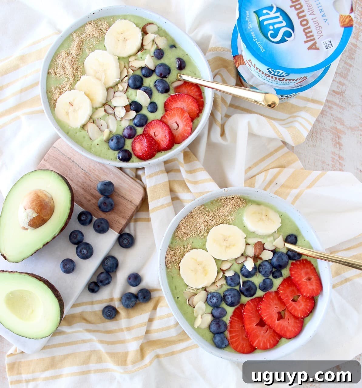 Two vibrant green avocado smoothie bowls, generously topped with fresh berries, sliced bananas, crunchy nuts, and chia seeds, inviting a healthy and delicious breakfast experience.
