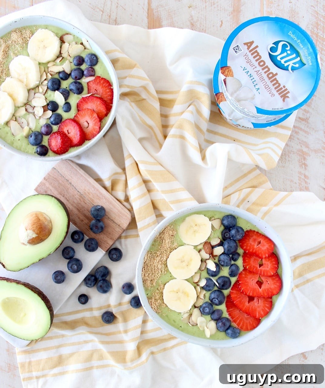 A close-up of a creamy green avocado smoothie bowl, artfully garnished with various colorful fruits like blueberries and raspberries, sliced kiwi, and a sprinkle of granola, showcasing its appealing texture and vibrant presentation.