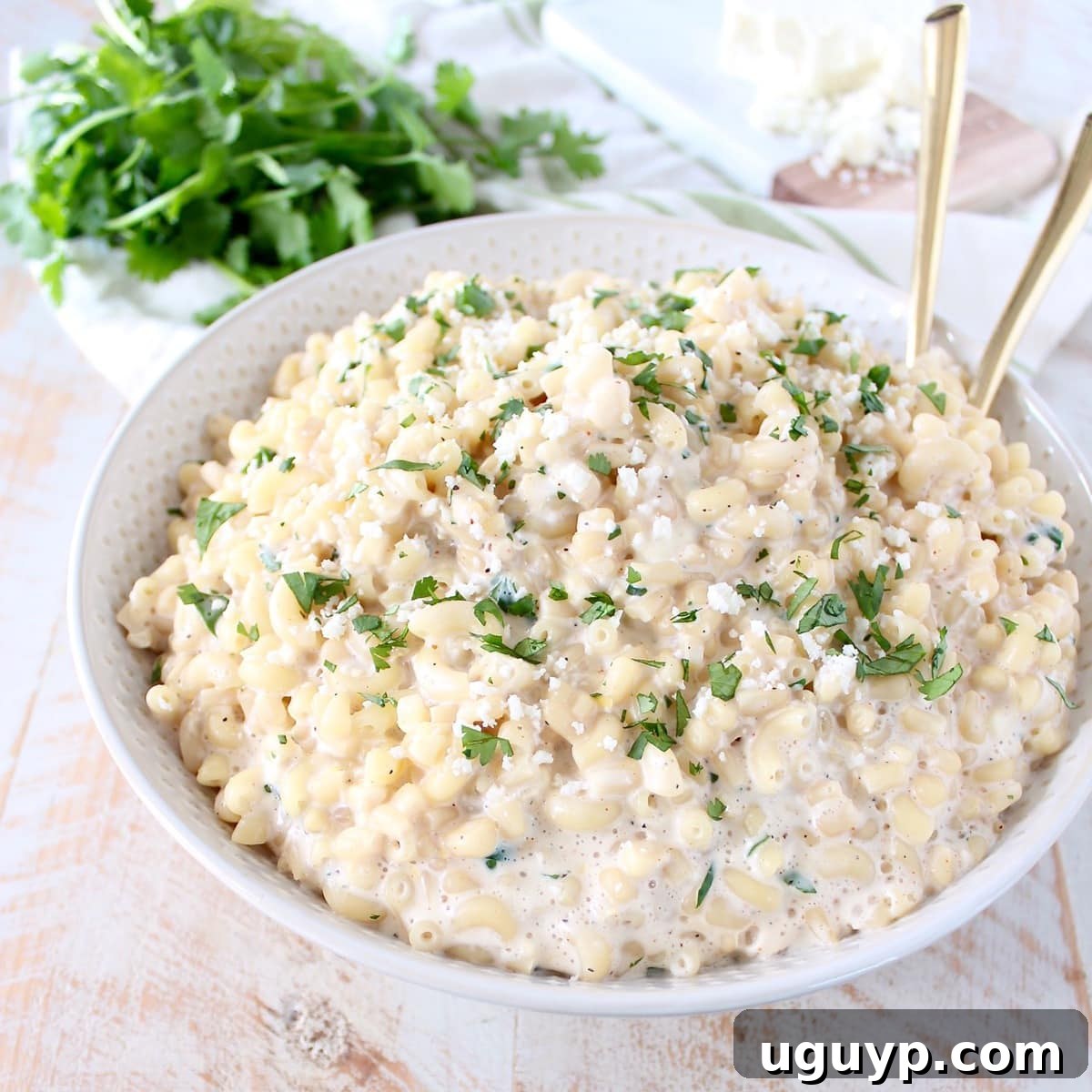 A beautifully presented bowl of Mexican street corn mac and cheese, accompanied by elegant gold serving spoons, highlighting its creamy texture.