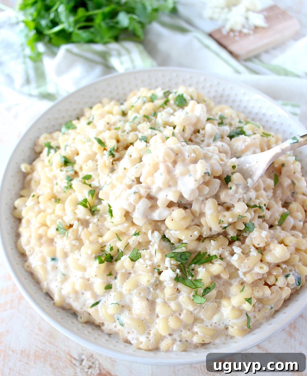 A close-up of Mexican street corn mac and cheese in a white bowl, with blurred green herbs in the background, emphasizing its freshness.