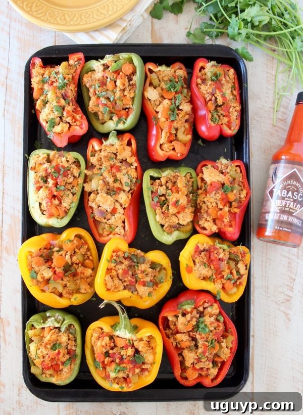 An appetizing overhead shot of buffalo chicken stuffed bell peppers on a baking sheet, with a bottle of buffalo sauce artfully placed beside them.