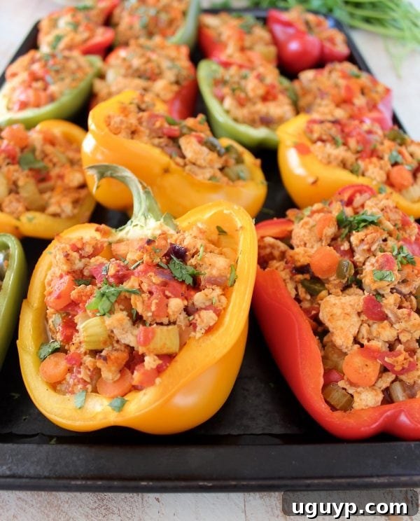 Cooked ground chicken, mixed with tender carrots and crisp celery, expertly stuffed into colorful bell pepper halves on a baking sheet.
