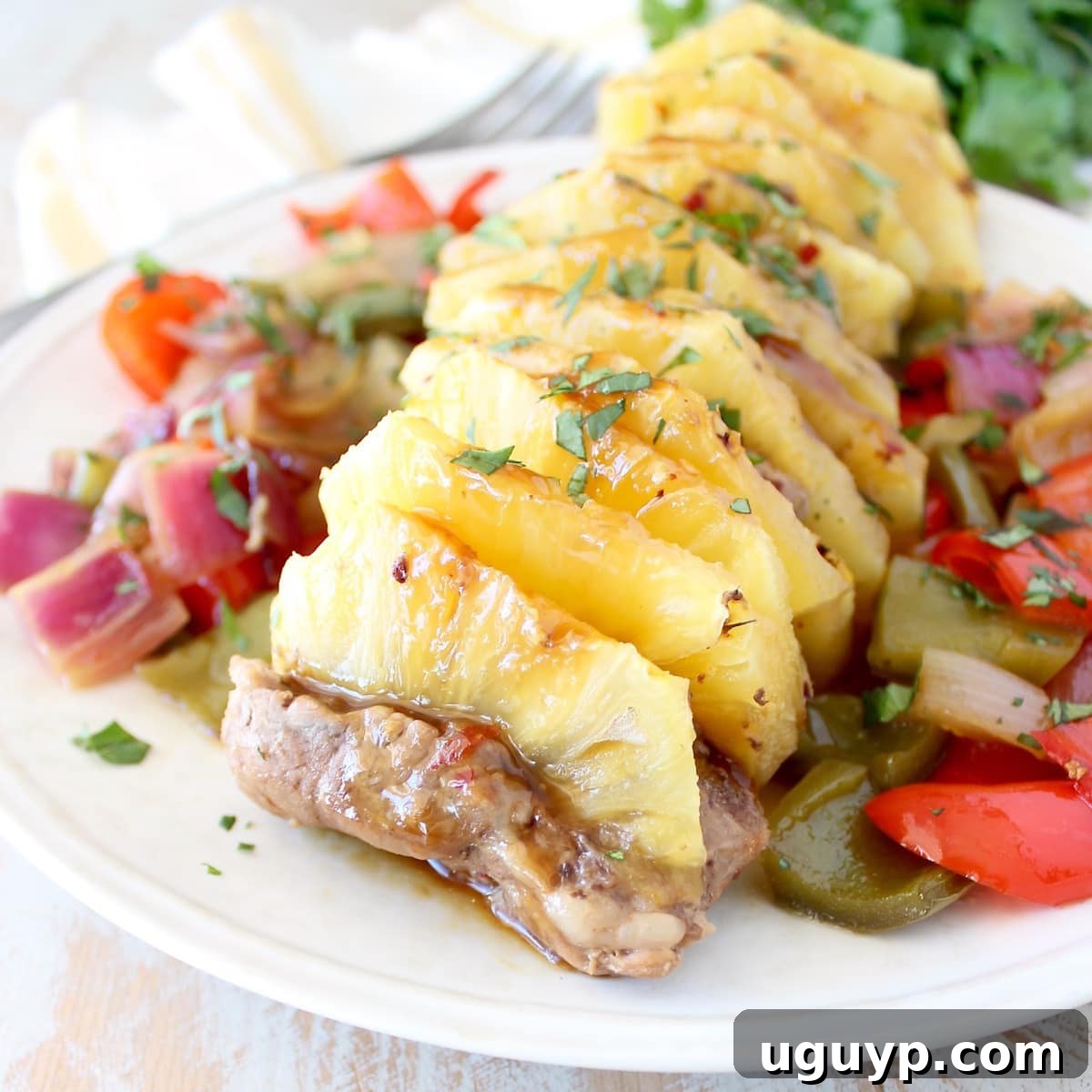 Cooked teriyaki pork tenderloin stuffed with pineapple slices, served with colorful bell peppers and onions