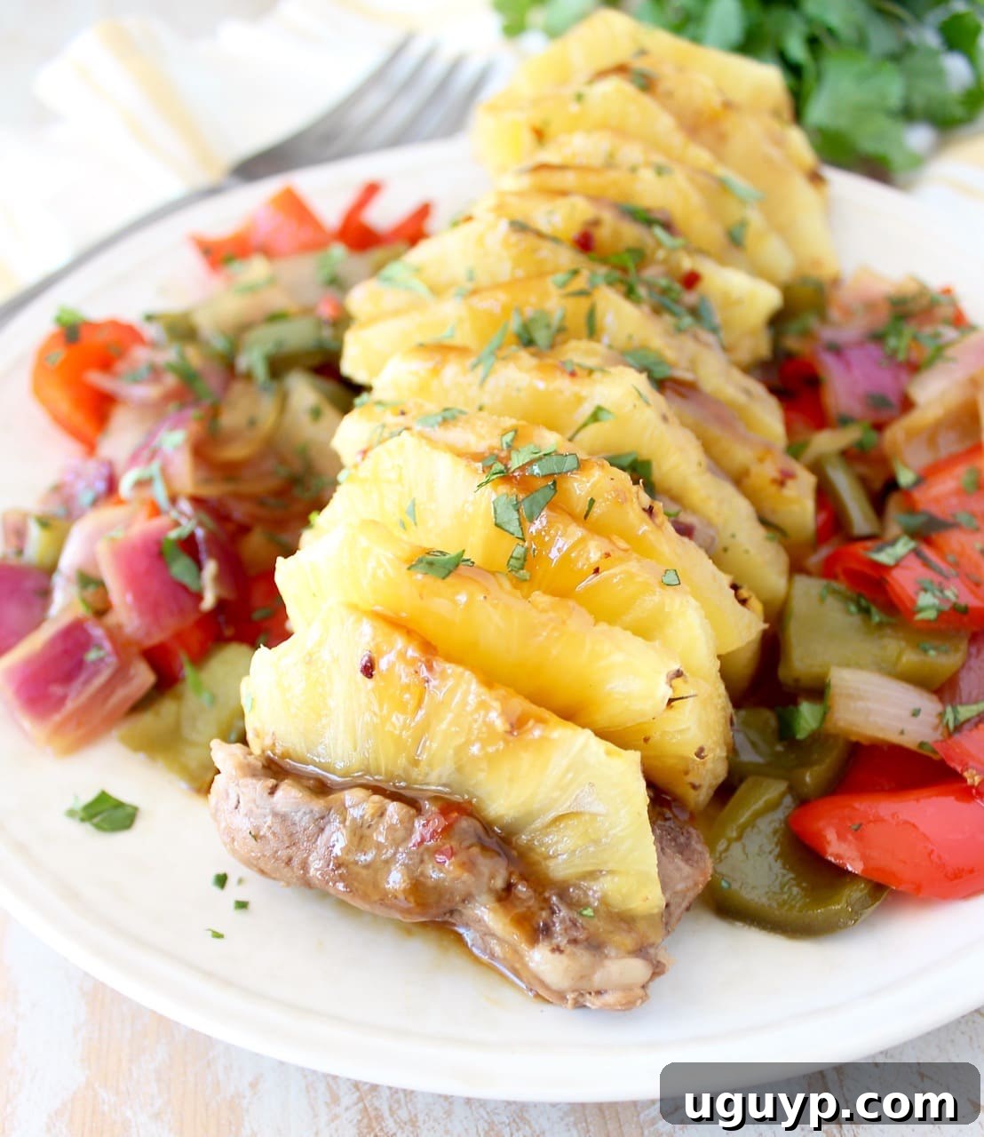 A plate of cooked pineapple teriyaki pork tenderloin, garnished with fresh herbs and surrounded by roasted bell peppers and onions.