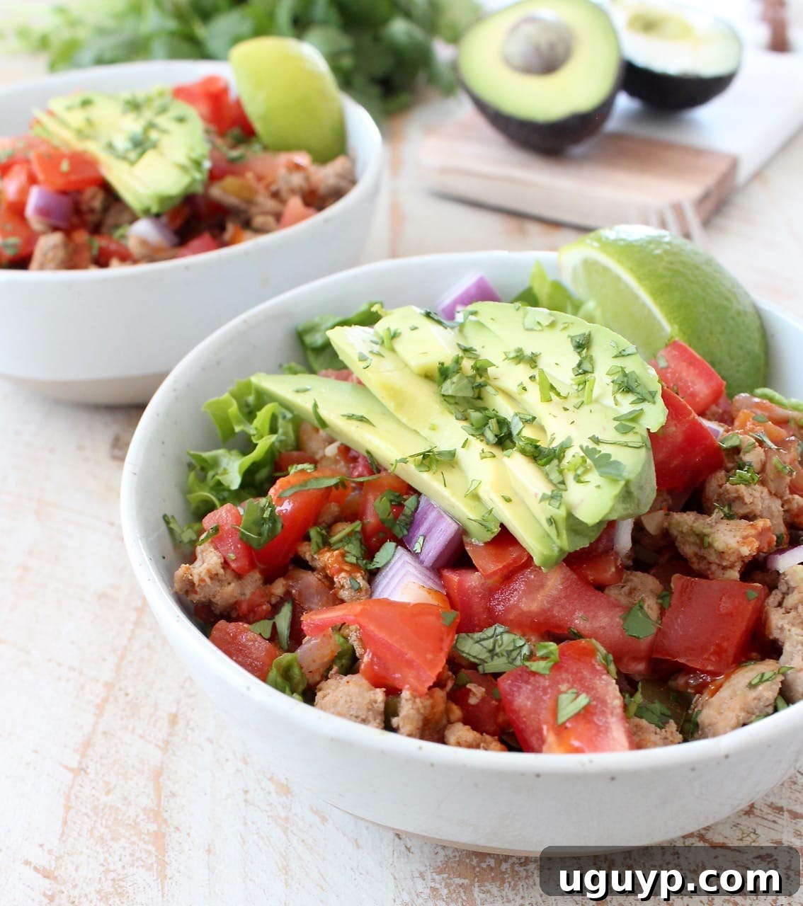 A refreshing white bowl filled with crisp lettuce, topped with a generous portion of taco-seasoned ground turkey, vibrant cooked peppers, onions, and diced tomatoes, alongside fresh avocado slices.