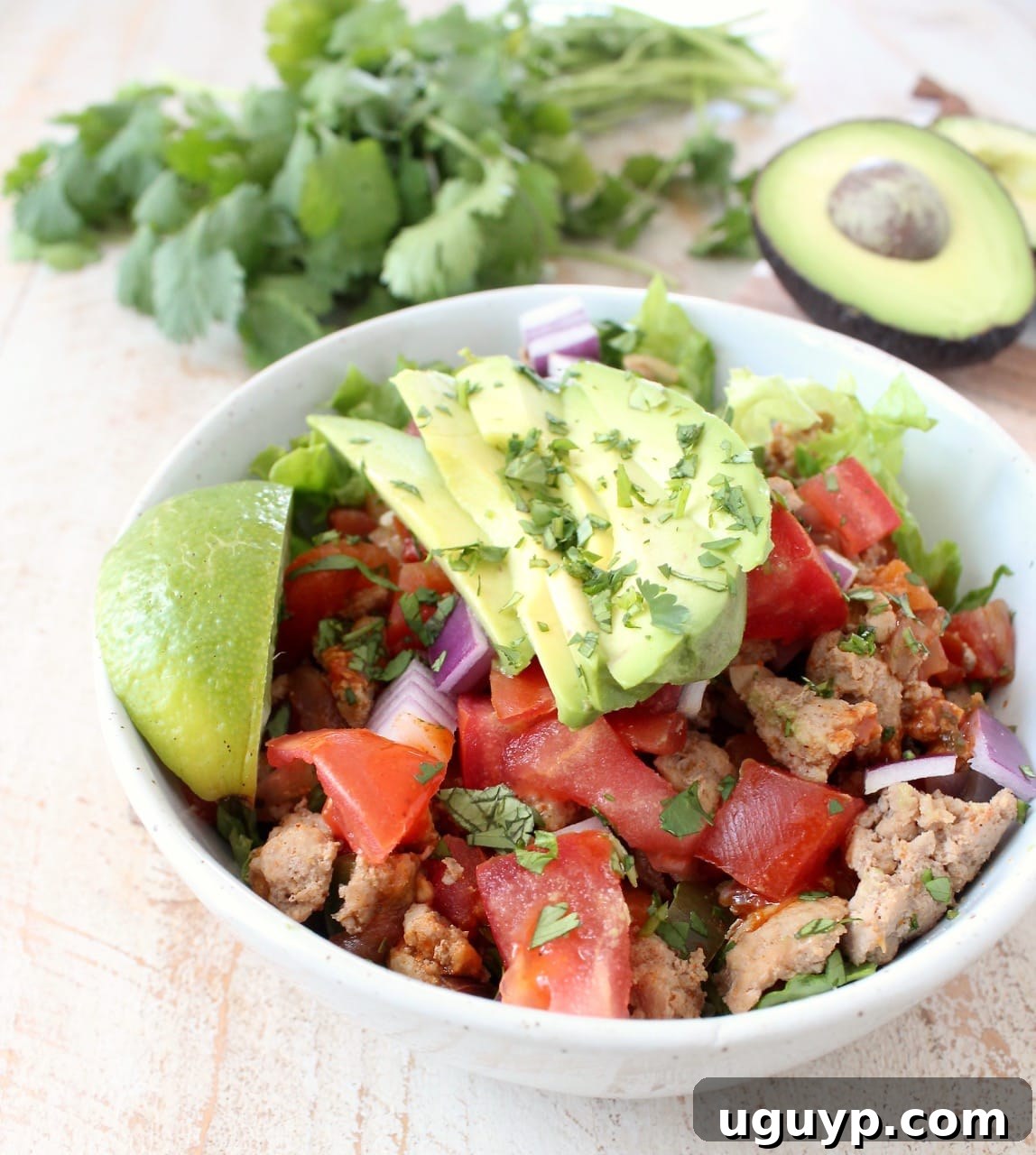 A close-up view of a wholesome Turkey Taco Salad in a white bowl, featuring seasoned ground turkey, vibrant peppers, onions, and tomatoes, elegantly arranged on a bed of fresh, crisp lettuce.