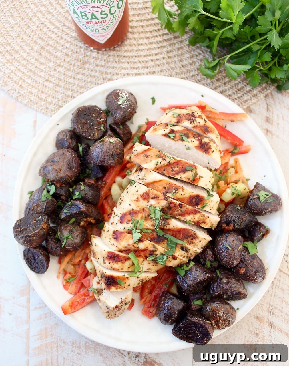 Sliced grilled chicken atop sliced bell peppers next to vibrant purple potatoes on a white plate, showcasing a complete and colorful meal.