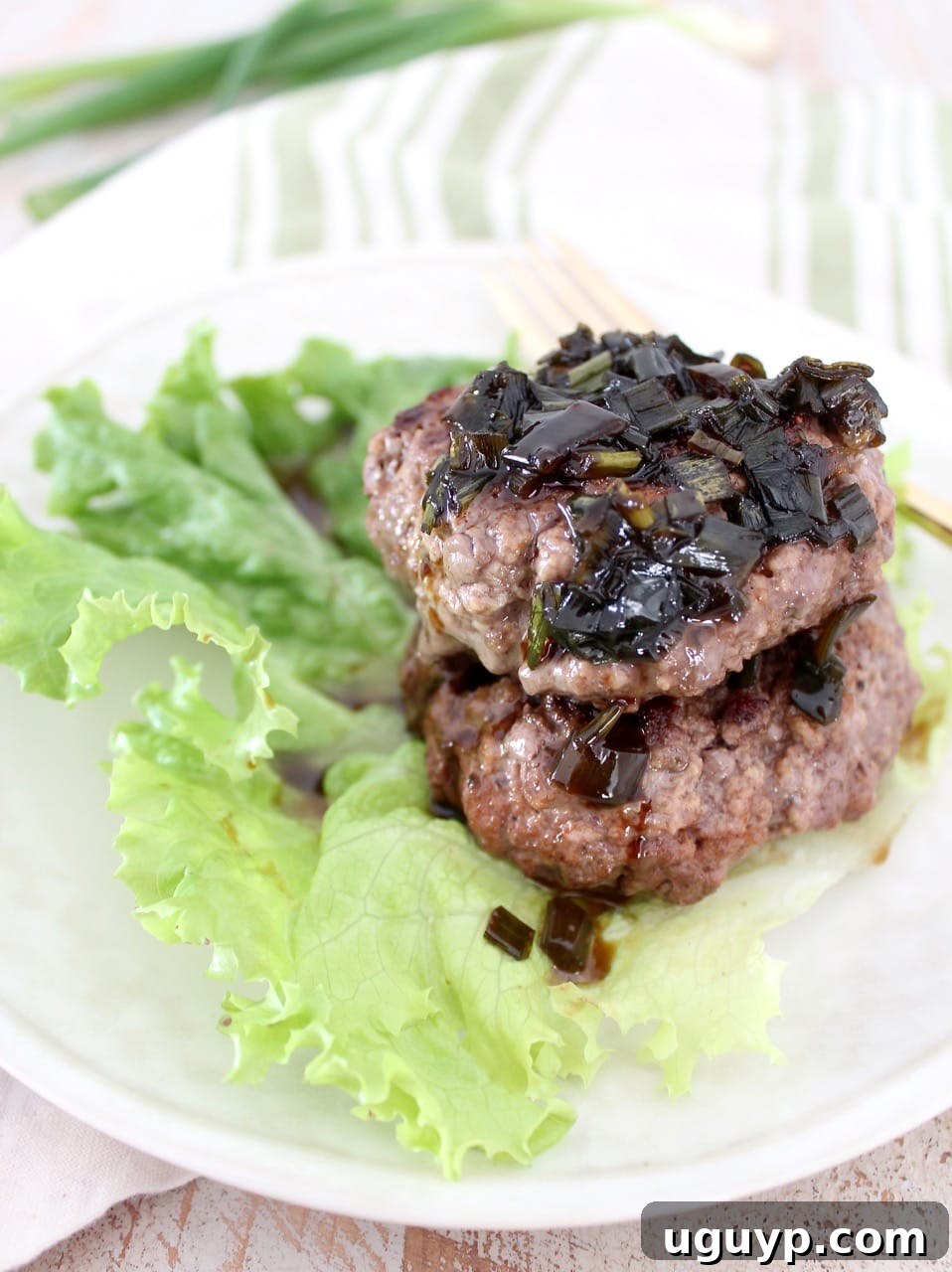 Two succulent Whole30 burger patties stacked on a fresh lettuce leaf, generously drizzled with a vibrant sesame scallion sauce, ready to be enjoyed.