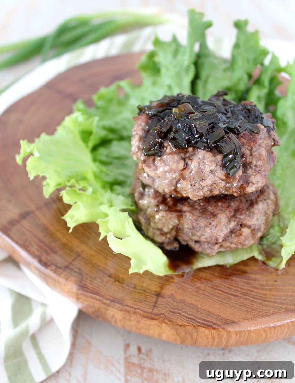 A vibrant close-up of two Whole30 burger patties, expertly stacked on a fresh lettuce cup and lavishly topped with the homemade sesame scallion sauce, showcasing its appealing texture and color.