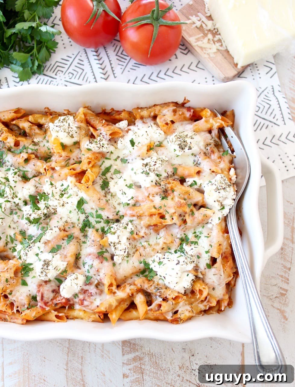 A large serving fork scoops a generous portion of cheesy baked ziti from a casserole dish, showcasing the layers of pasta, sauce, and melted cheese, ready to be enjoyed.