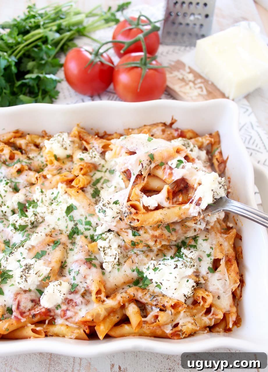 Close-up of baked ziti in a ceramic casserole dish, showcasing the bubbling melted mozzarella and ricotta cheese over a rich tomato sauce, garnished with fresh herbs.