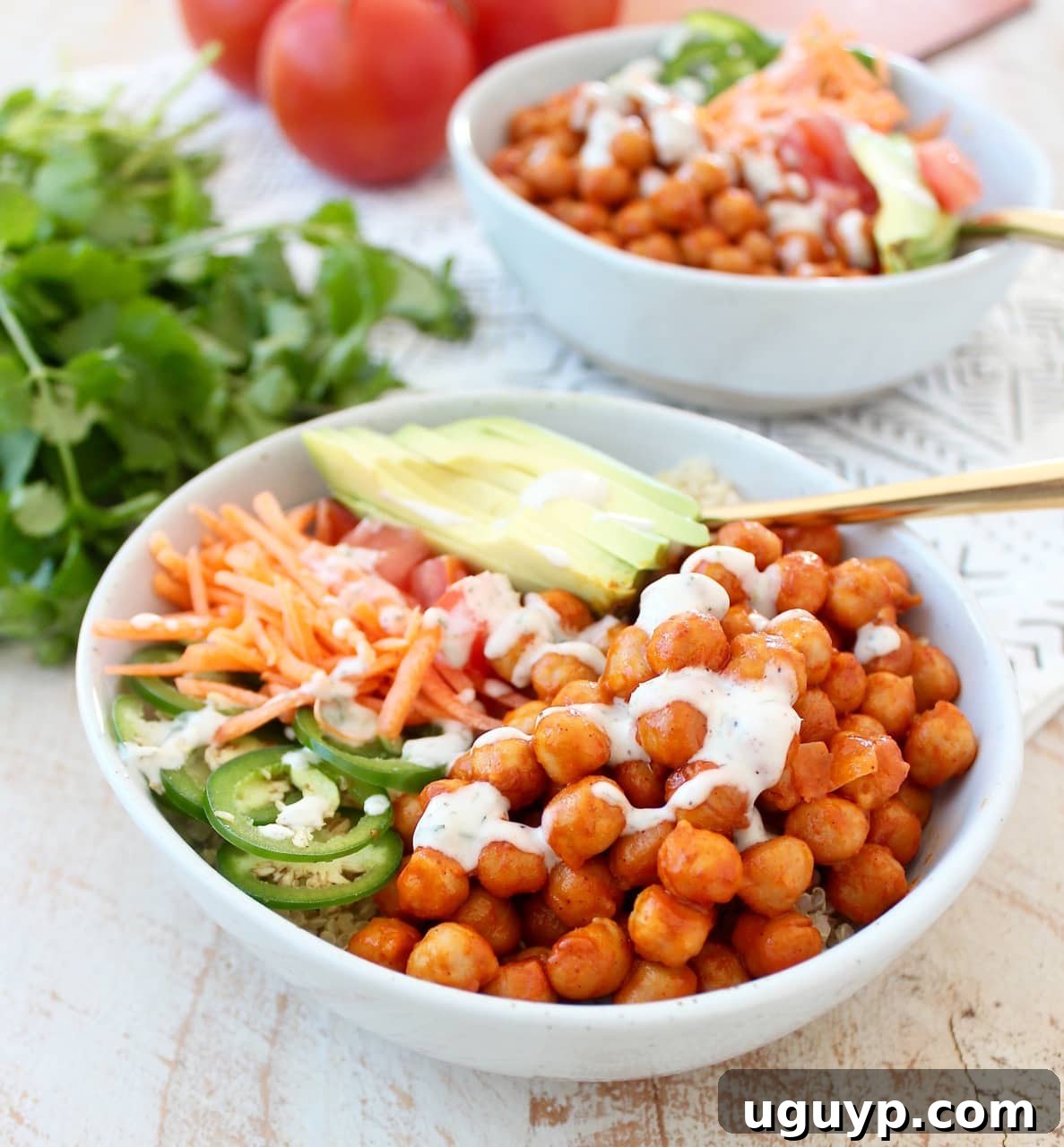 A close-up of a single bowl filled with buffalo chickpeas, quinoa, sliced carrots, diced tomatoes, and avocado, with a gold fork resting in the bowl.