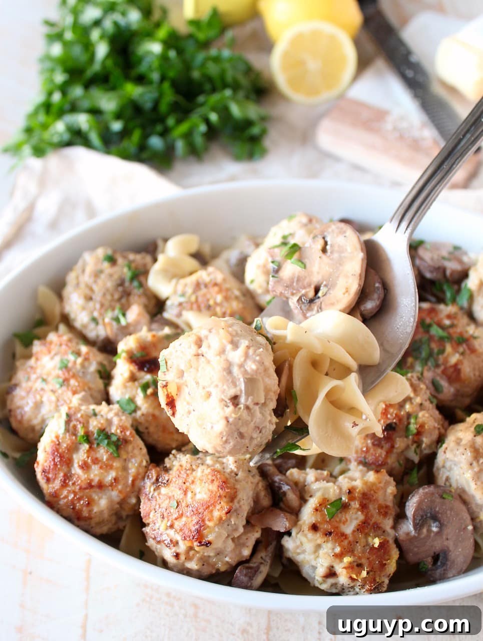 A serving fork lifting a tender chicken marsala meatball, surrounded by creamy sauce, mushrooms, and noodles, from a casserole dish.