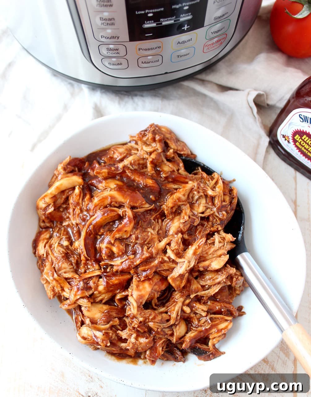 Shredded chicken coated in BBQ sauce in a white bowl with a spoon, ready to be served or used in other recipes.