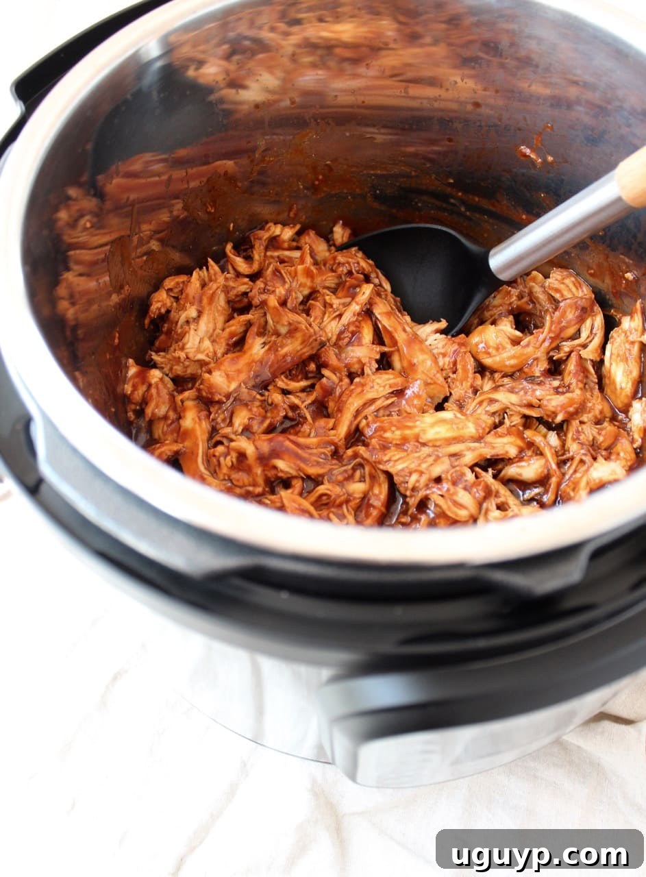 Shredded BBQ chicken fresh from the Instant Pot, with a serving spoon resting inside the pot.