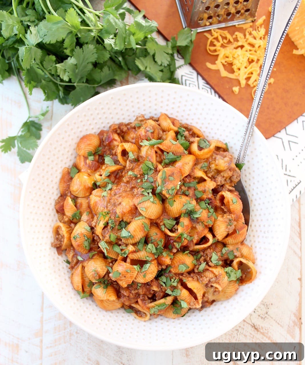 Overhead view of a large bowl of Enchilada Pasta, garnished with fresh cilantro and a dollop of sour cream, with a serving spoon resting in the dish.