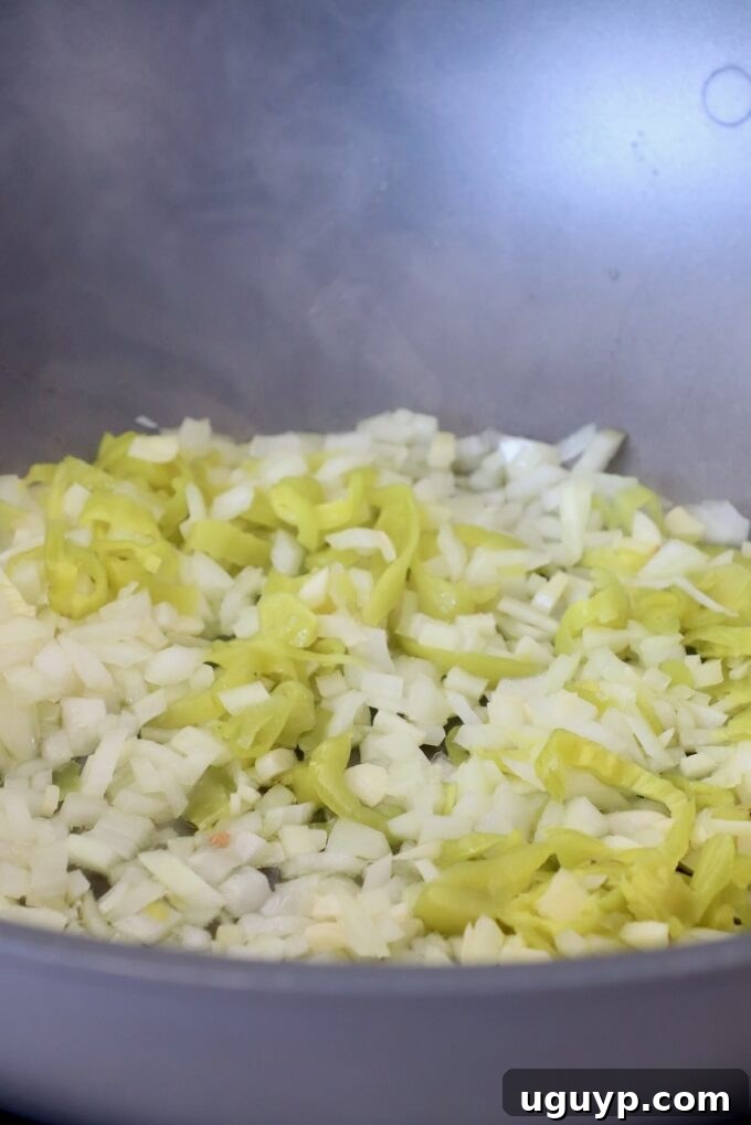 Diced onions and sliced pepperoncinis are sautéing in a large pan with olive oil, beginning to soften and become fragrant.