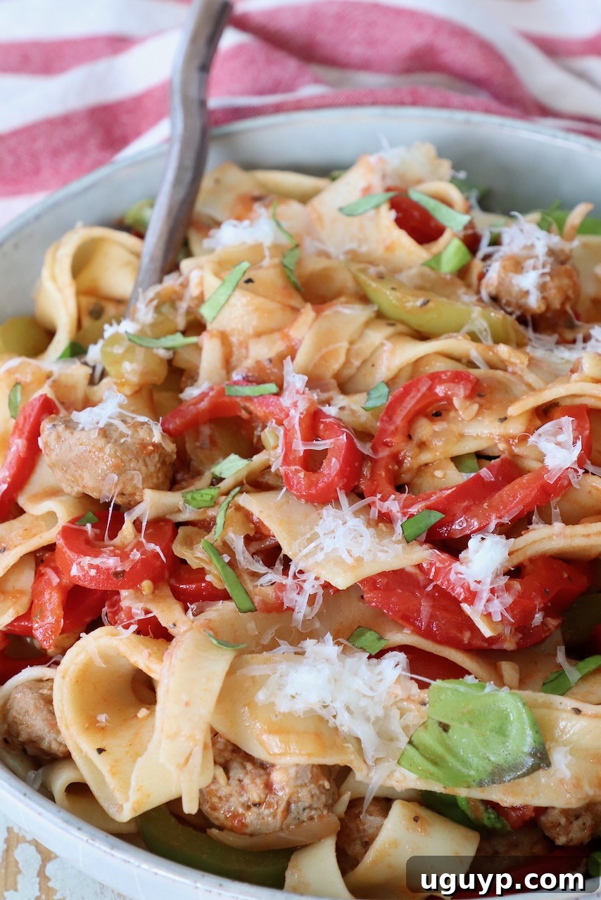 A close-up of a serving of Italian Drunken Noodles in a bowl, showing the wide pasta, colorful peppers, sausage, and fresh basil, ready to be enjoyed.