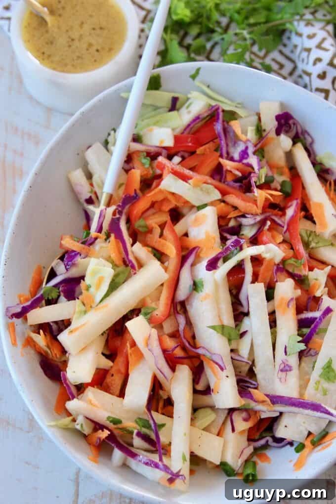 Close-up of Jicama Coleslaw in a rustic bowl with a serving spoon, highlighting its fresh ingredients and vibrant colors.