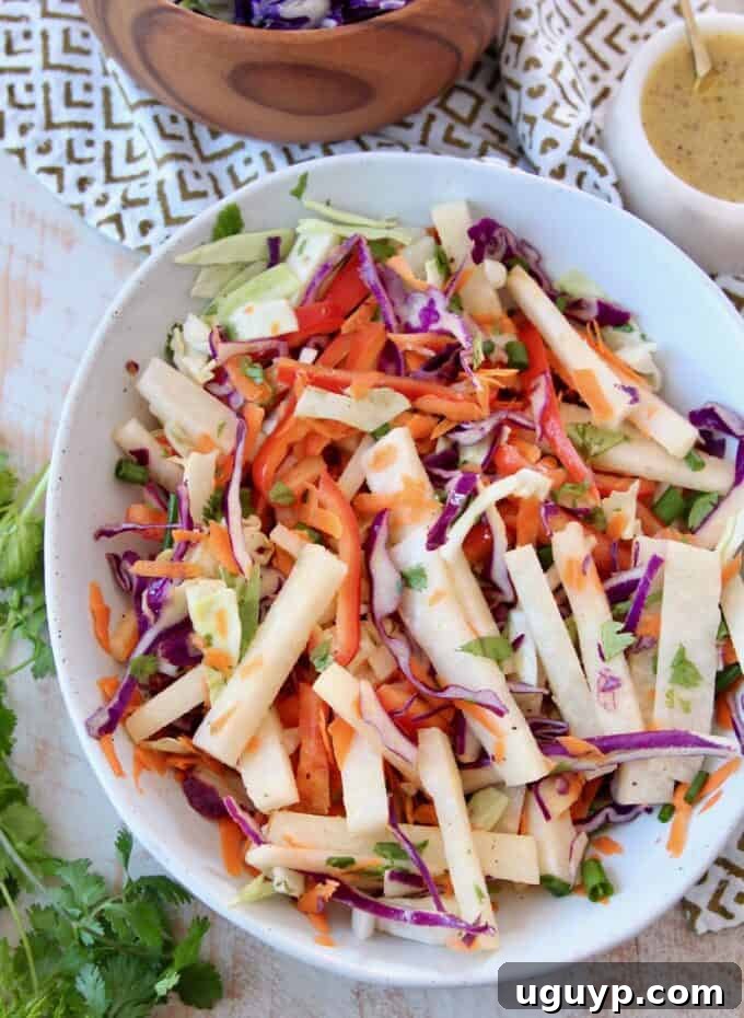 Jicama Slaw in a bowl with ingredients for its vinegar dressing on the side, emphasizing its light and healthy nature
