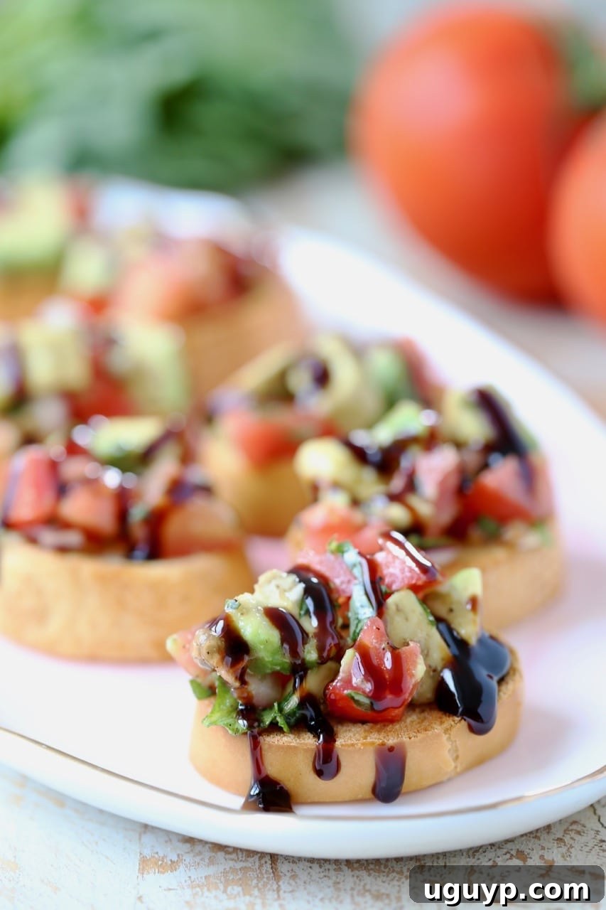 Diced avocado and tomato mixture beautifully arranged on toasted baguette slices, artfully drizzled with balsamic reduction, presented on a rustic plate.