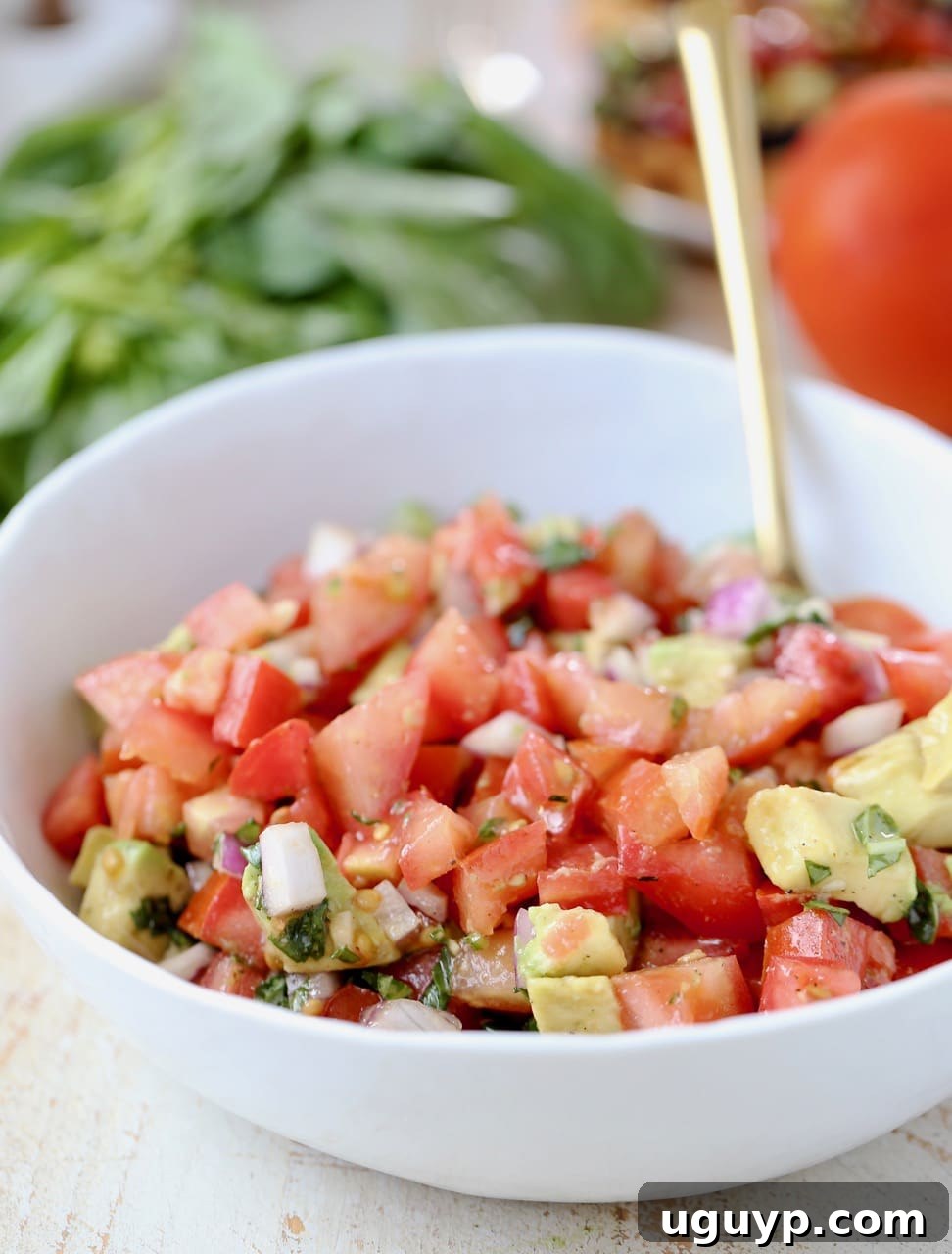 A close-up shot of freshly diced tomatoes, red onions, and ripe avocado, perfectly mixed together in a pristine white bowl, awaiting assembly onto toasted bread.
