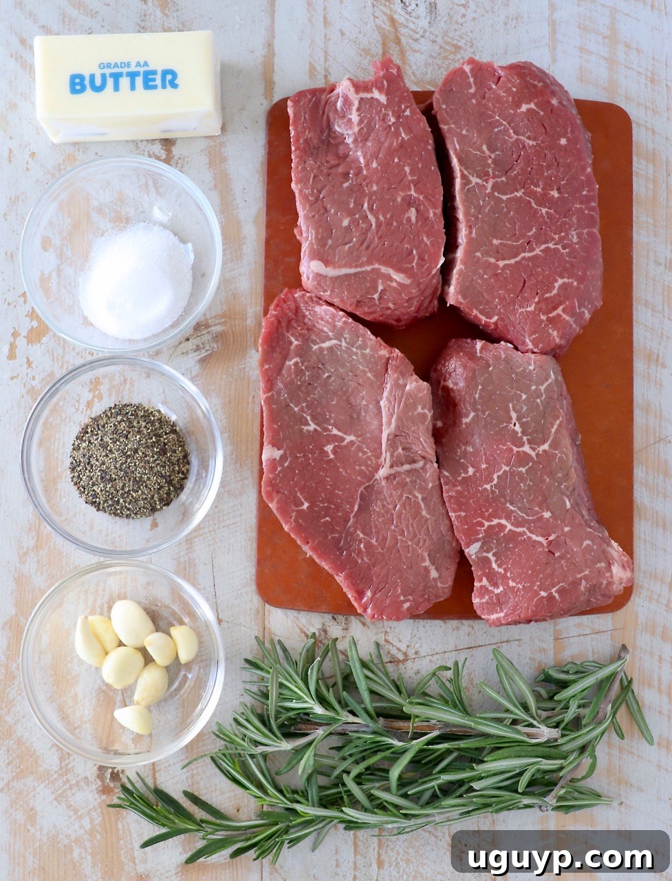 Sous vide sirloin steak ingredients laid out on a cutting board, including fresh rosemary, garlic, salt, pepper, and butter.