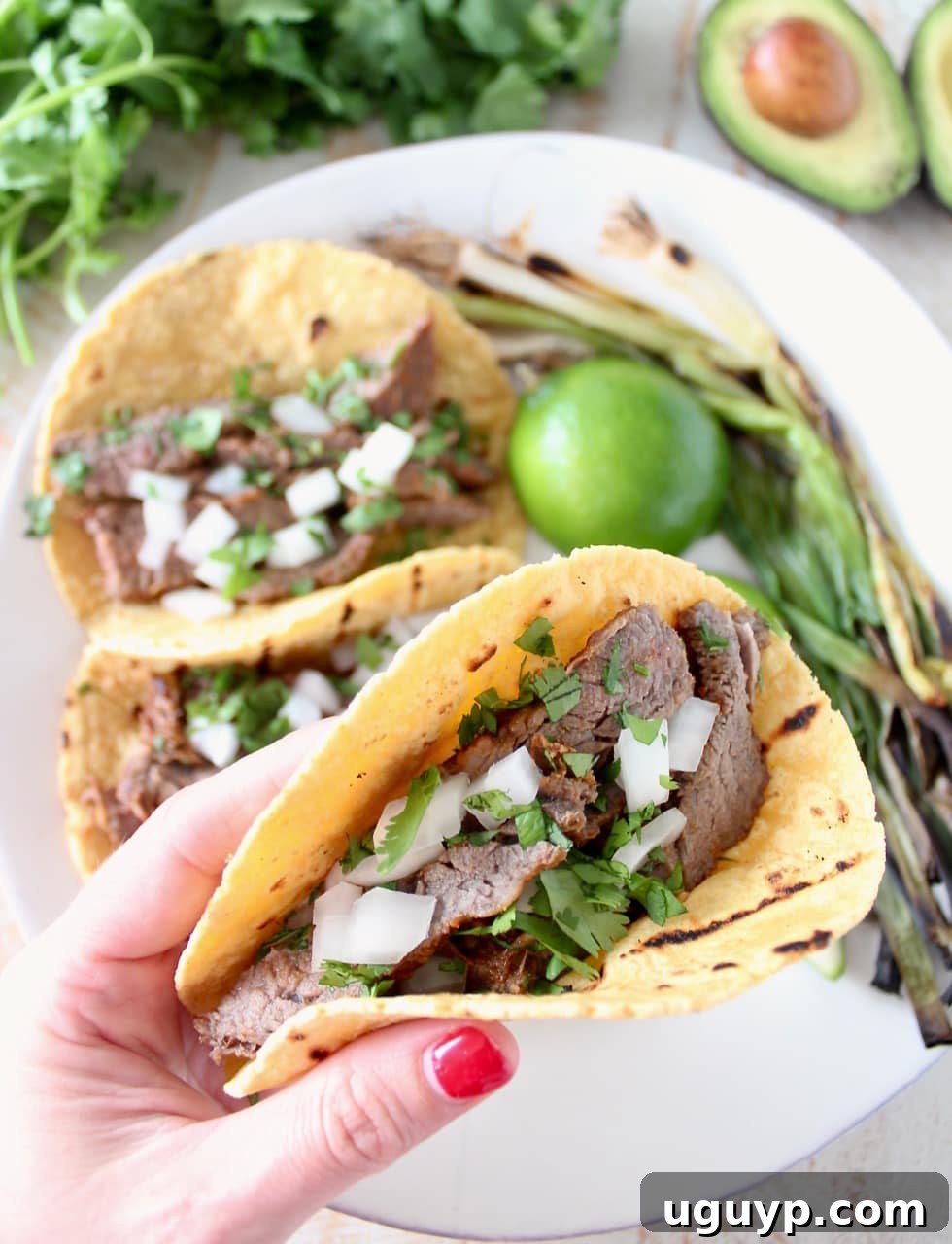 Flavorful Carne Asada Tacos adorned with fresh cilantro, diced red onions, and grilled green onions, served on warm corn tortillas.