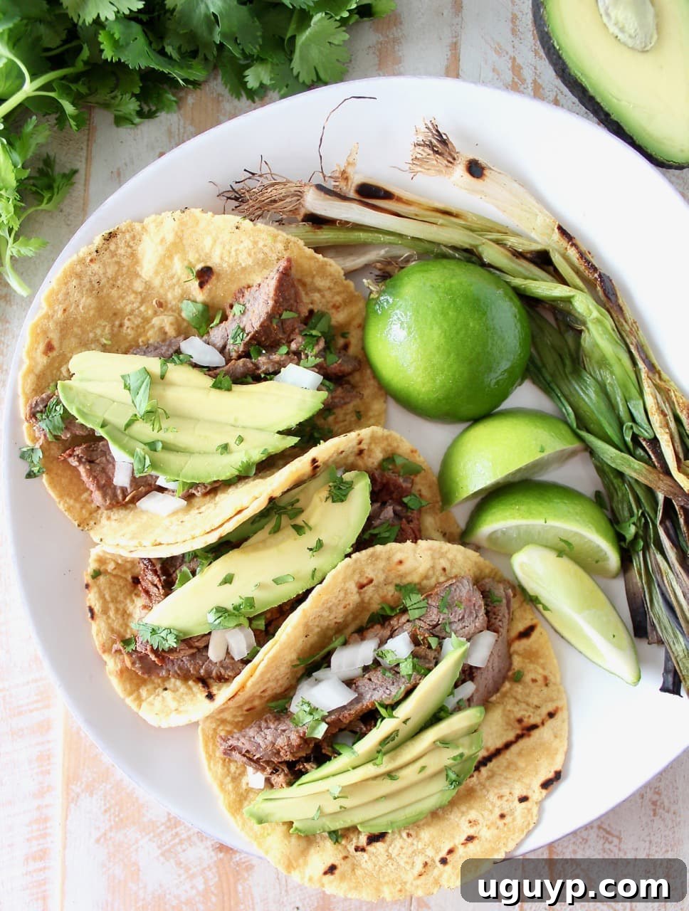 Carne Asada Taco recipe presented with fresh limes, creamy avocado slices, and vibrant red onions, highlighting the freshness of the ingredients.