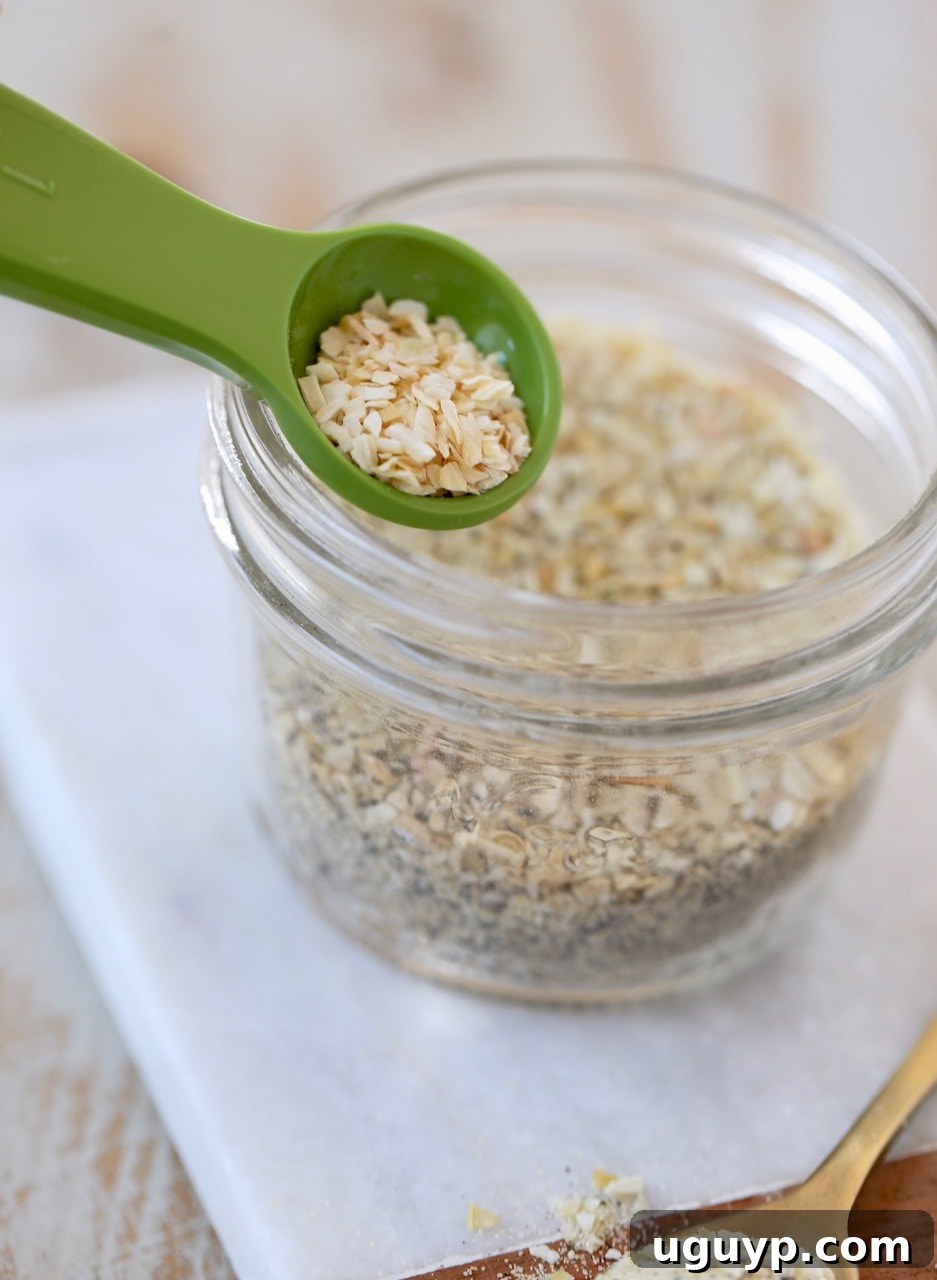 French Onion Dip Mix stored neatly in a clear mason jar, with a green measuring spoon scooping out dried minced onions, symbolizing the fresh, organized approach to homemade seasoning.