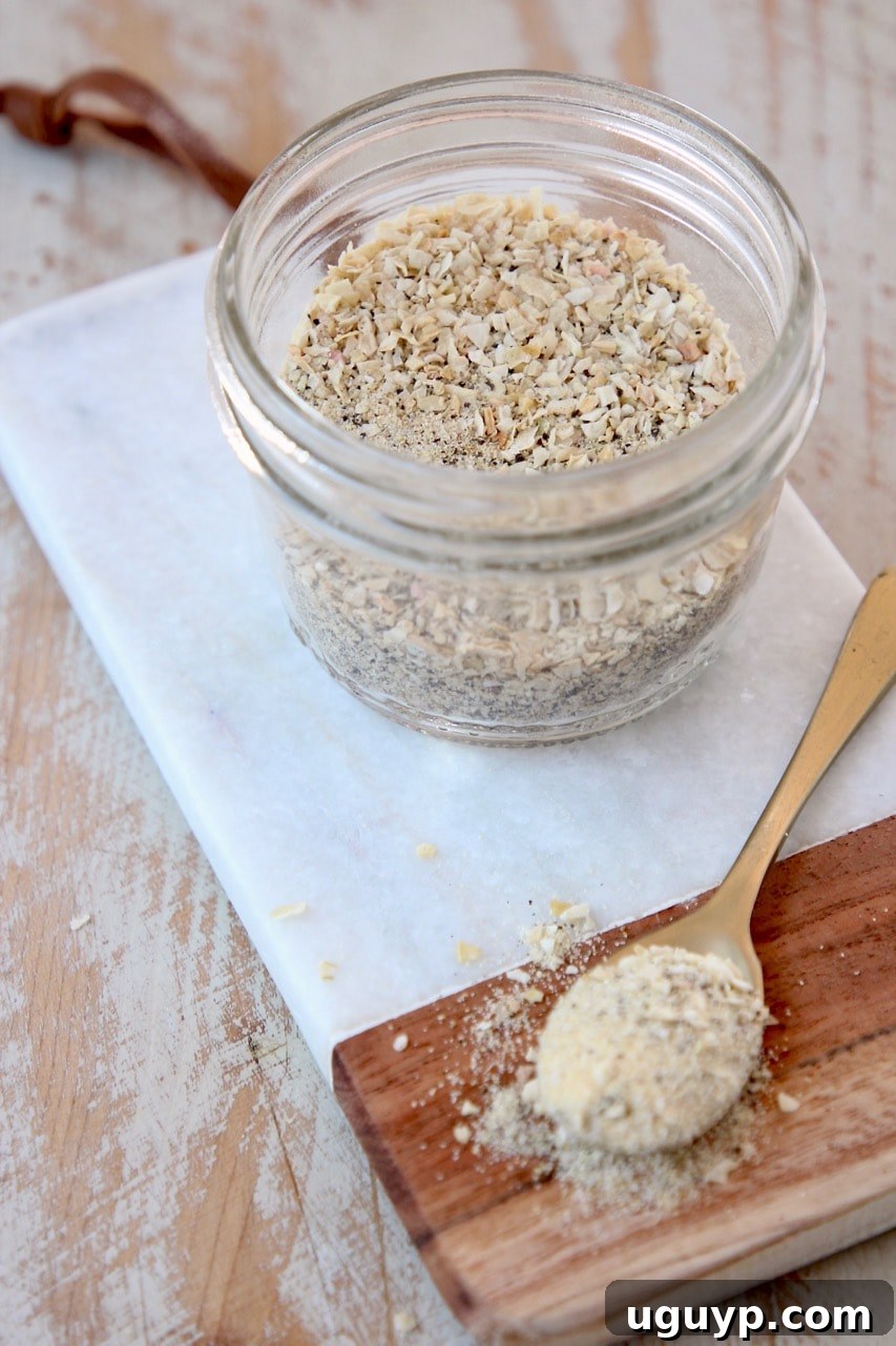 A mason jar filled with homemade French Onion Dip Mix, accompanied by a golden spoon holding a sample of the mix, elegantly displayed on a surface, ready to be used or stored.